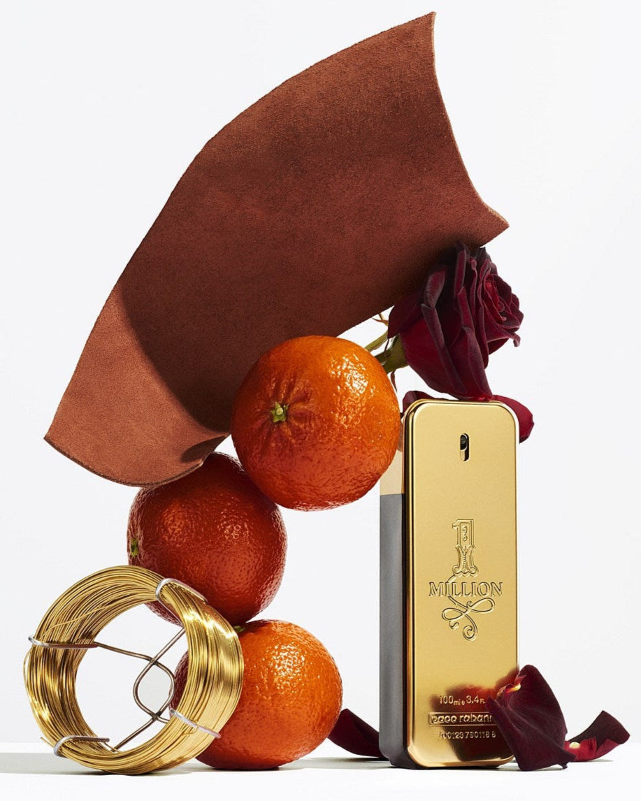 1 Million Gold perfume bottle with oranges, leaves, and a red flower on a white background