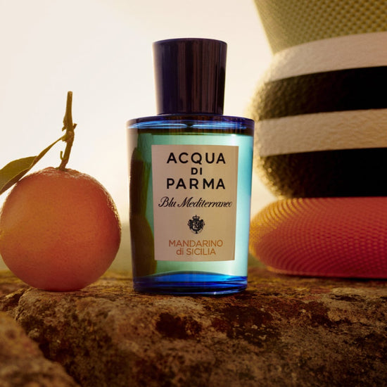 Acqua di Parma bottle with an apricot and a hat on a stone surface