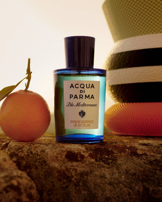 Acqua di Parma bottle with an apricot and a hat on a stone surface